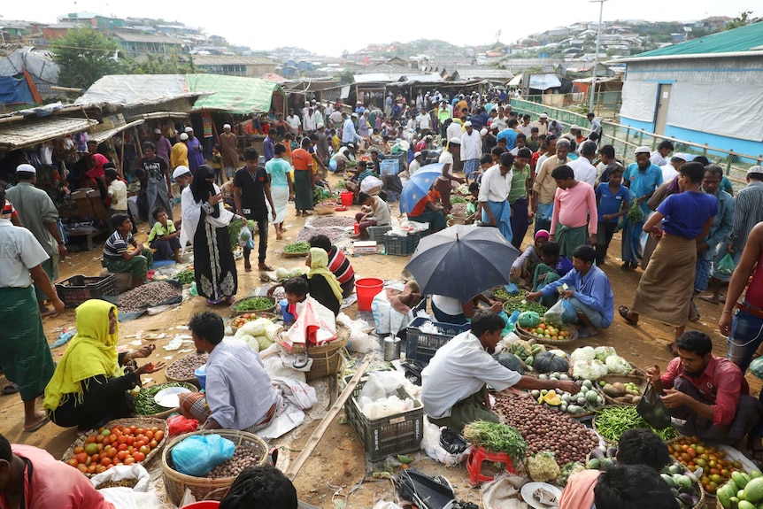 A busy market with umbrellas and fruit laid out on the ground as people mill around at Cox's Bazar refugee camp.