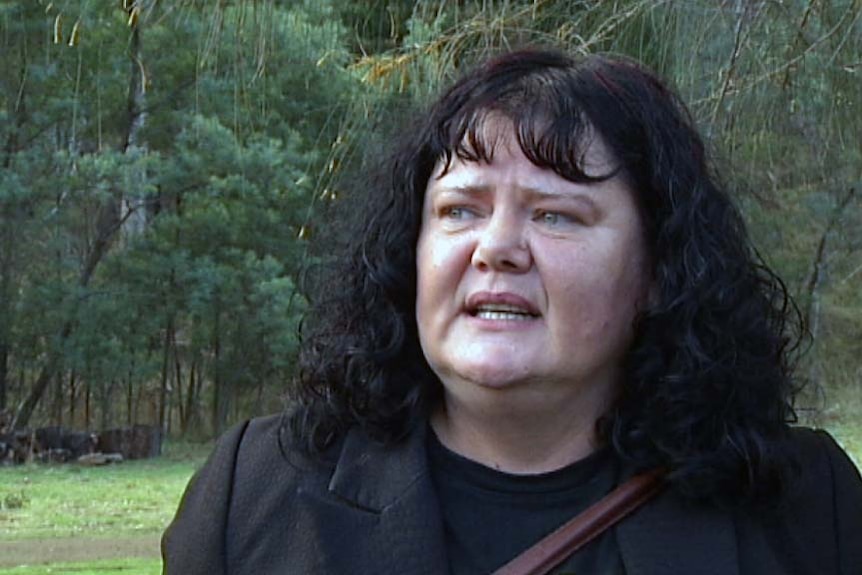 Trudy Maluga speaks in front of trees.