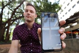A young man holds his phone close to the camera. A government message can be seen saying 'no bookings available'.