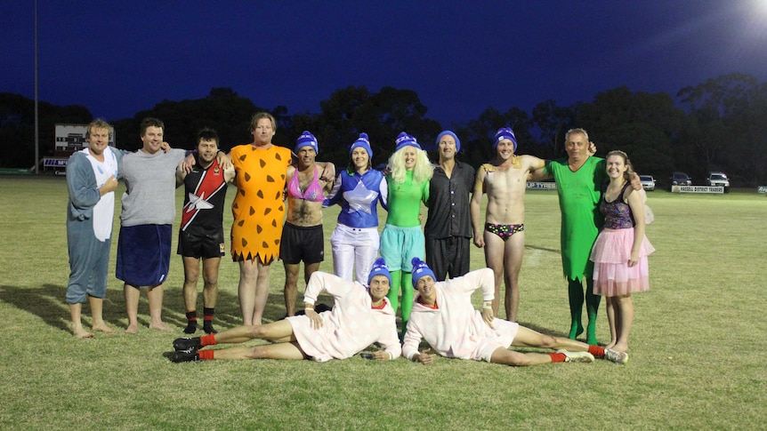 A group of people in fancy dress stand on a football oval after taking the icy plunge to raise money for MND research.