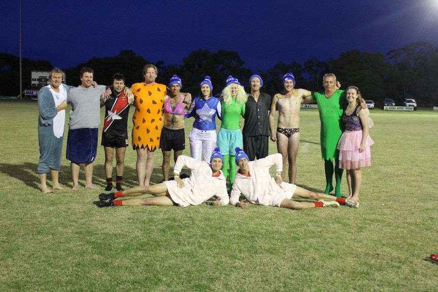 A group of people in fancy dress stand on a football oval after taking the icy plunge to raise money for MND research.