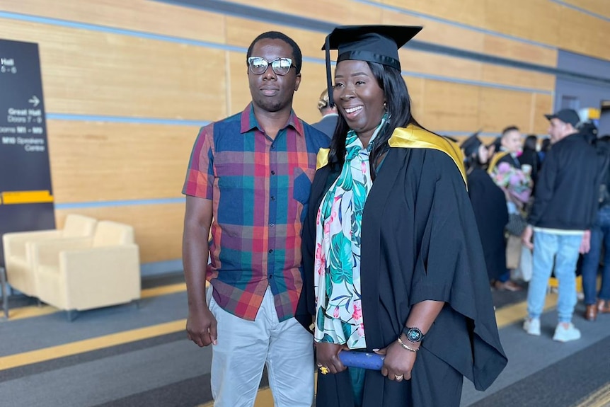 a woman dressed in tertiary graduation garmets smiling while standing next to her adult son