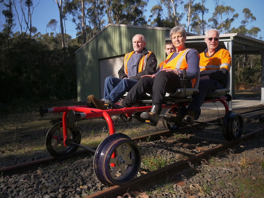 Four people sitting on a red rail bug, looking ready to pedal.