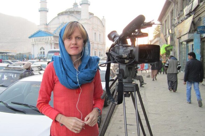 Woman wearing headscarf standing next to camera on tripod in Kabul street.