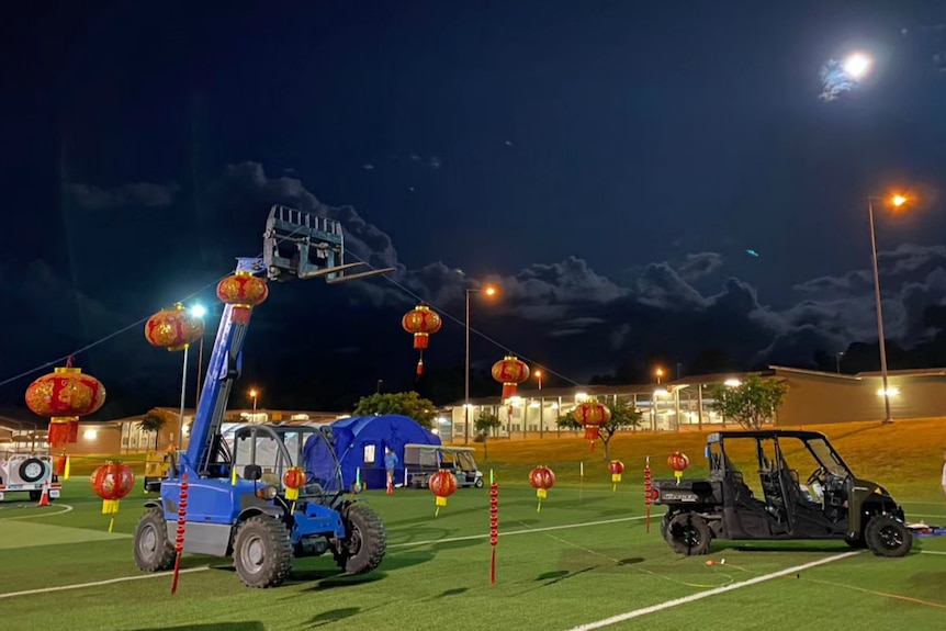 A string of red lanterns, hung across a green sports field, at night.