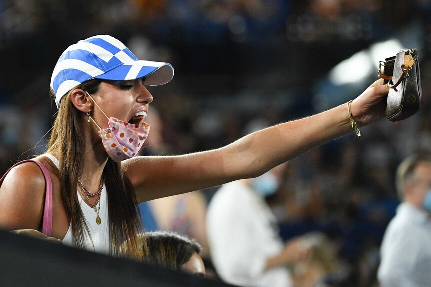 A spectator wearing a cap in the colours of the Greek flag stands in the Rod Laver Arena crowd.