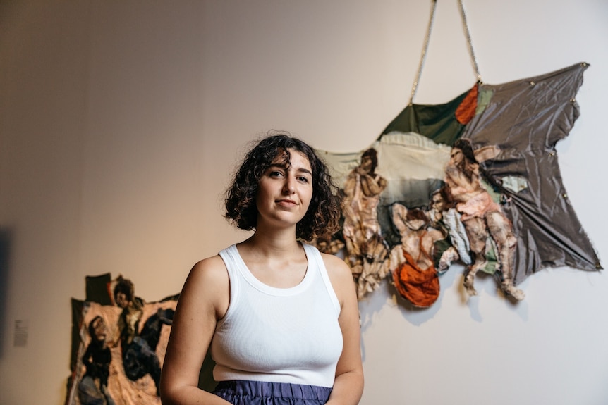 Julia Gutman stands with a slight smile in front of her Ramsay Art Prize entry, a textile installation of people at the beach