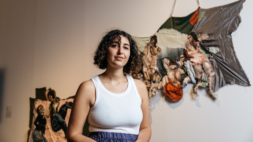 Julia Gutman stands with a slight smile in front of her Ramsay Art Prize entry, a textile installation of people at the beach