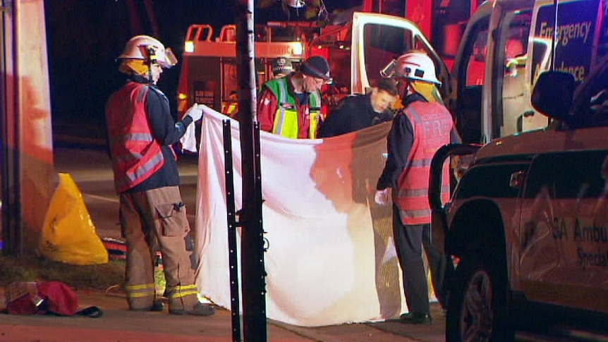 Emergency services hold up a sheet as other work at the scene of a fatal crash.