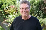 A man with glasses with green plants in the background