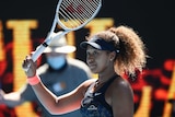 A tennis player raises her racquet in acknowledgement of crowd after a win at the Australian Open.