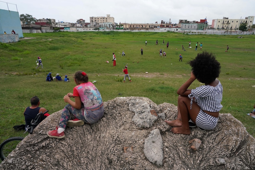 Las niñas miran desde una roca alta un juego de béisbol para niños