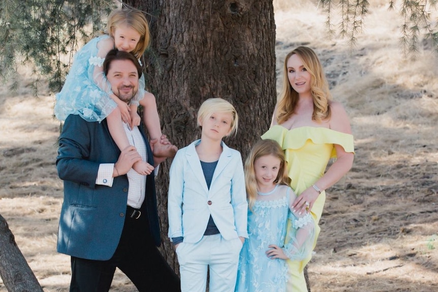 A man and a woman pose for a portrait in front of a tree with their three children.