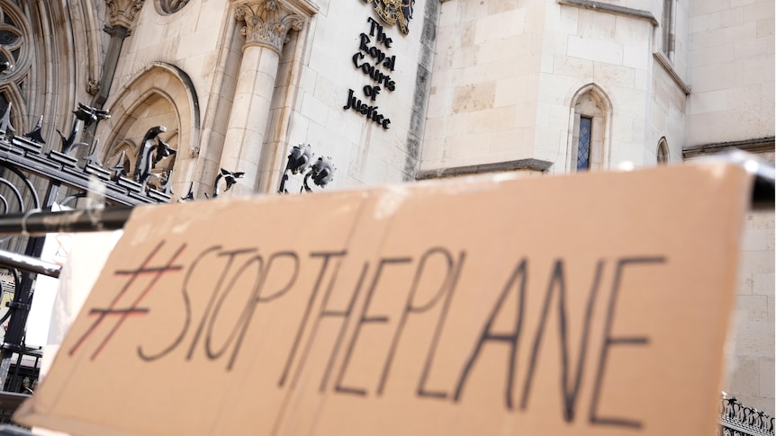 A cardboard sign being held outside the High Court saying "stop the plane".