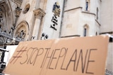 A cardboard sign being held outside the High Court saying "stop the plane".