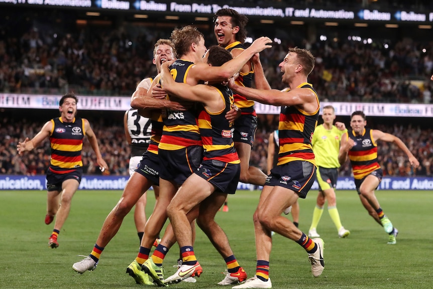 Adelaide Crows players jump on and run to hug Jordan Dawson after a winning goal against Port Adelaide.