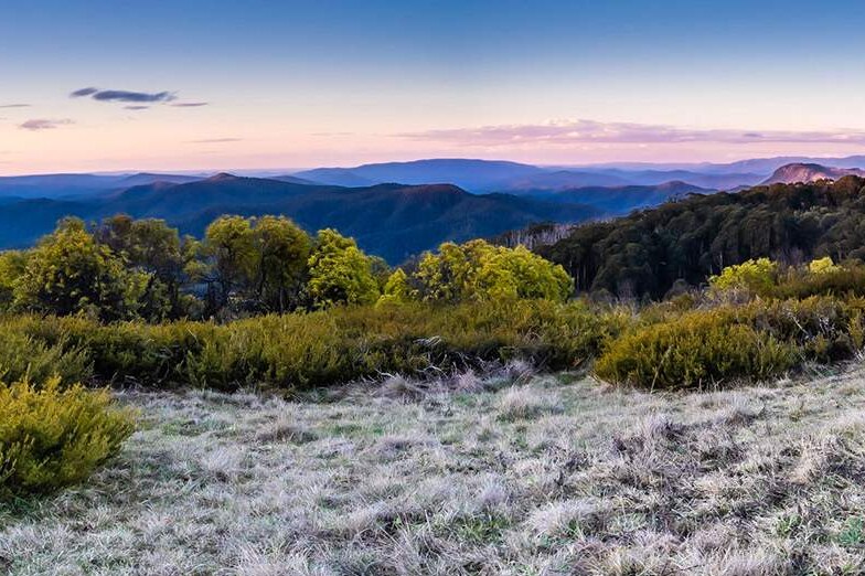 A scenic photograph shows bushland and rolling mountains at dawn or dusk.