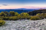 A scenic photograph shows bushland and rolling mountains at dawn or dusk.