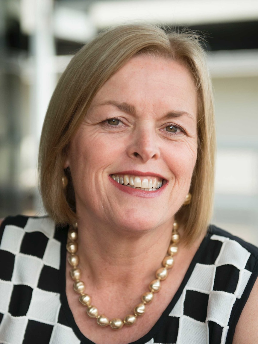 Photo of Karen Flanagan, wearing pearl earings and necklace, black and white checked shirt.