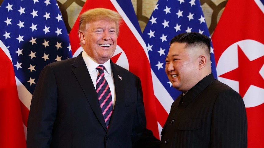 President Donald Trump laughs alongside Kim Jong-un in front of US and Korean flags.
