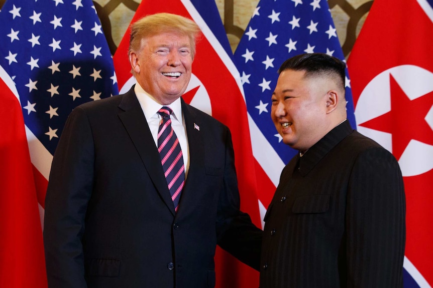 President Donald Trump laughs alongside Kim Jong-un in front of US and Korean flags.