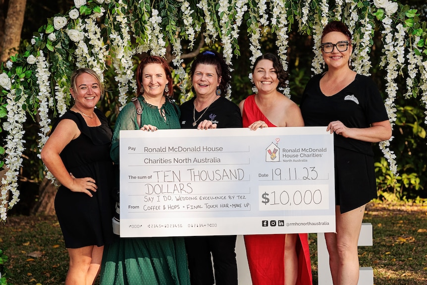 Five women stand smiling behind a giant cheque reading $10,000 for Ronald McDonald Charities
