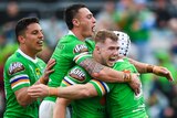 Four Canberra Raiders NRL players embrace as they celebrate scoring a try against the Warriors.