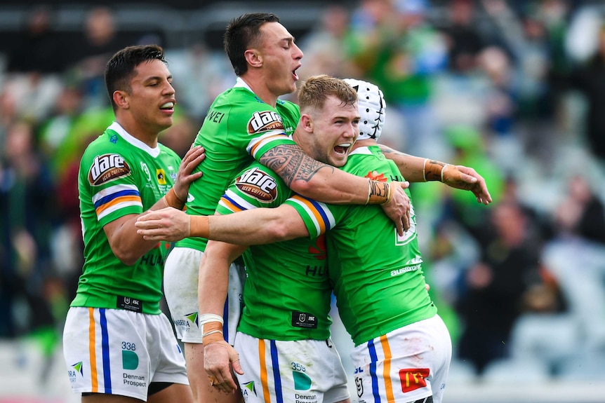 Four Canberra Raiders NRL players embrace as they celebrate scoring a try against the Warriors.