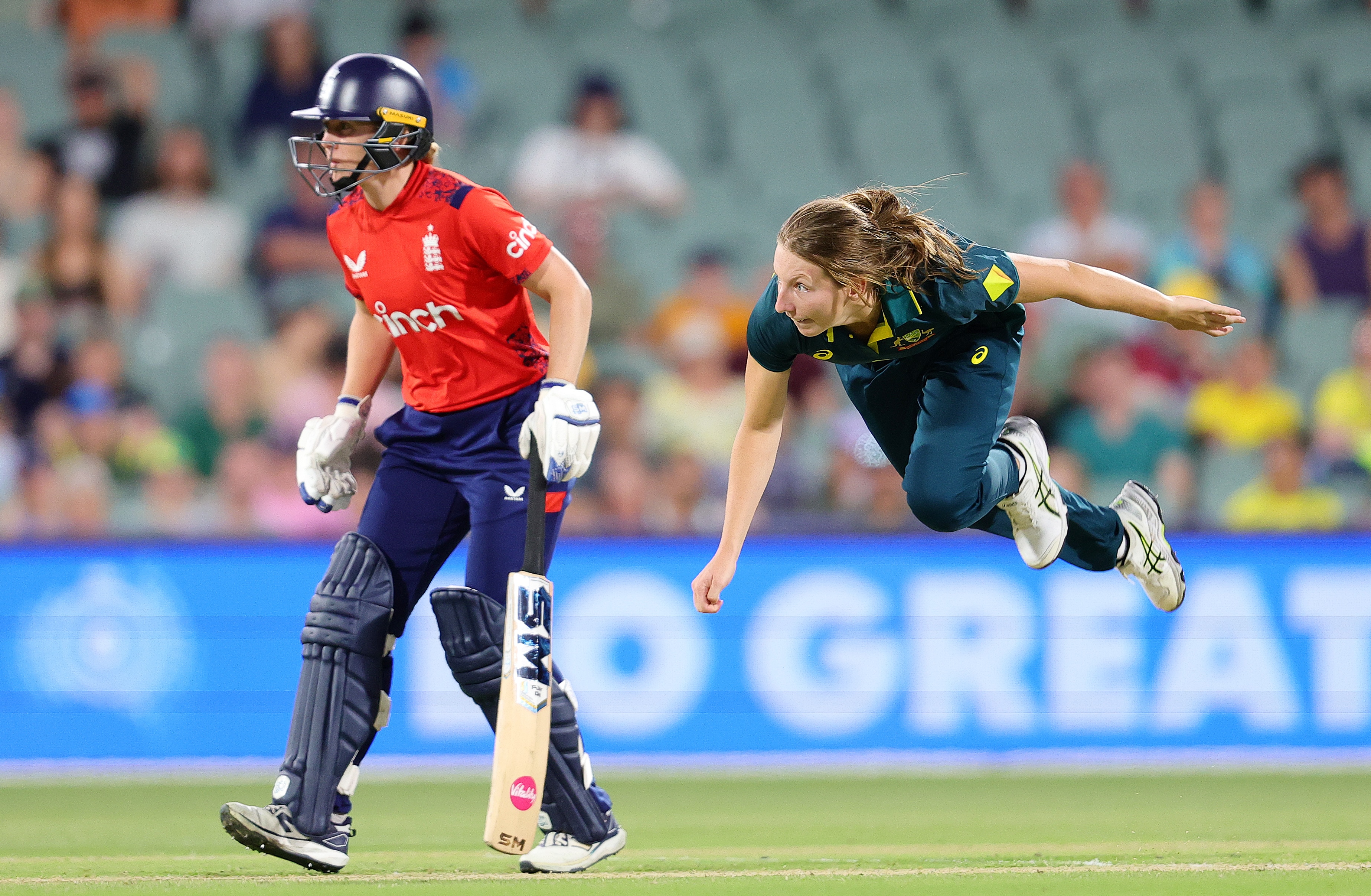 Darcie Brown appears to be in mid-air as she completes a delivery while an England batter stands near her