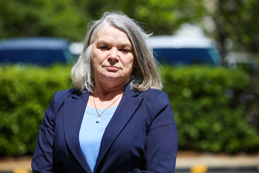 A woman wearing a navy blue jacket and grey hair stands in a courtyard