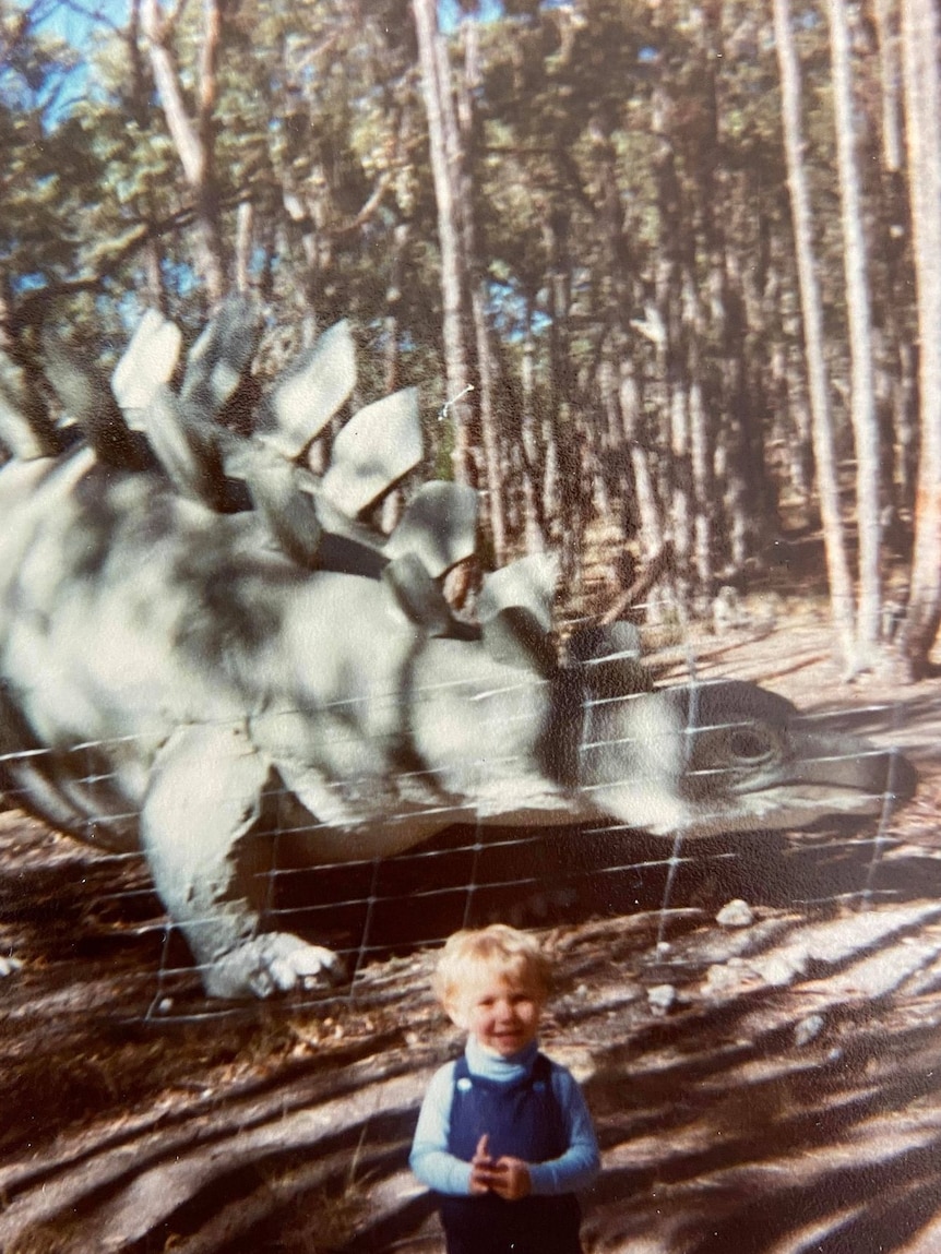 Un jeune garçon se tient devant un modèle de dinosaure en riant 