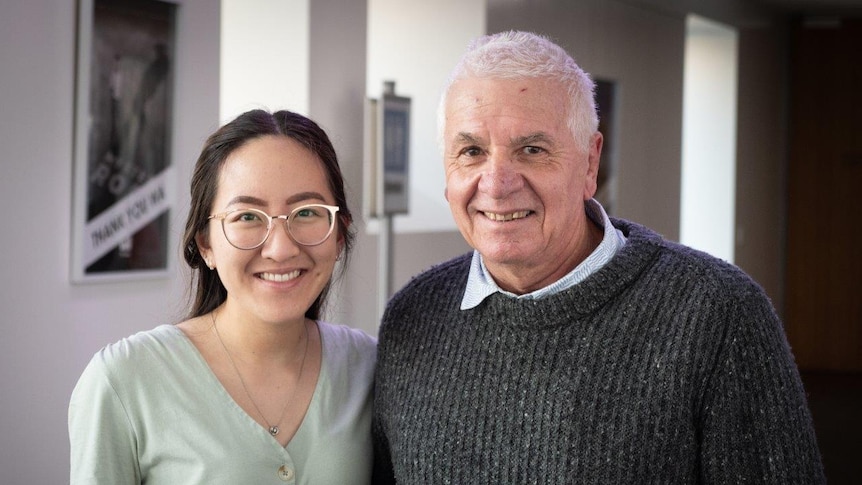 A young woman with glasses and an older man with short grey hair smile at the camera