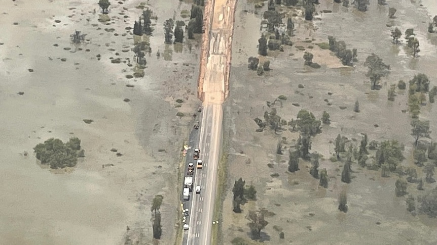 An aerial shot of a road surrounded by floodwaters, a large section of bitumen is washed away