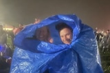 Two people with a tarp wrapped around them at a concert outside.