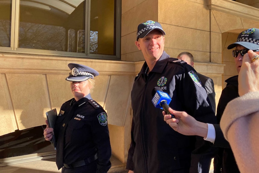 Three police officers in uniform (one female, two male). The middle is looking at the camera.