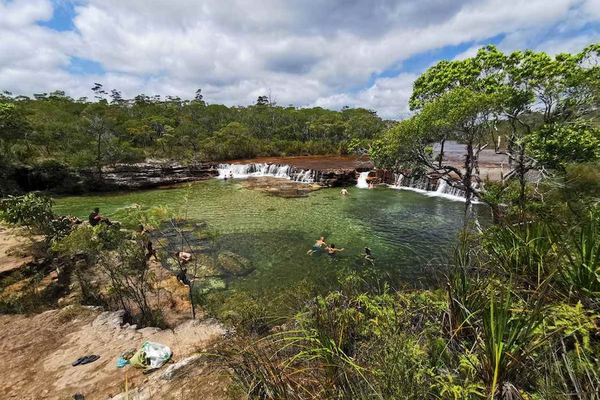 Photo of low, wide waterfall with people swimming