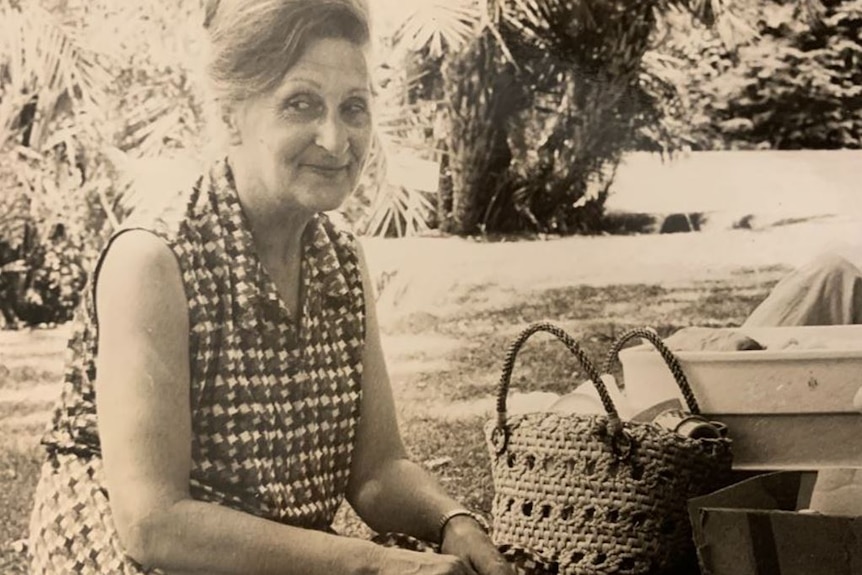 Black and white image of a middle aged woman sitting on a picnic rug outdoors