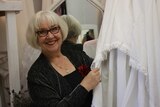 Mauzie Chau holds the hem of a wedding dress hanging in a room full of white gowns.