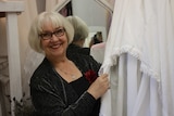 Mauzie Chau holds the hem of a wedding dress hanging in a room full of white gowns.