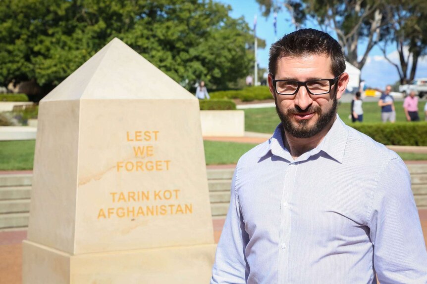 Gary Wilson stands in front a monument reading 'Lest we forget Tarin Kot, Afghanistan.'