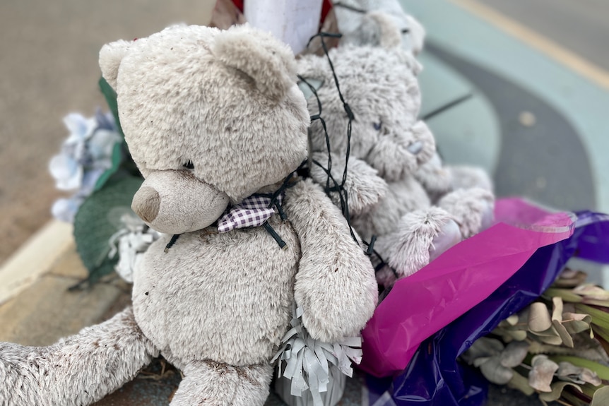 grey teddy bears and a bouquet of flowers tied to a traffic pole with ferry lights mark the traffic island Will was crossing