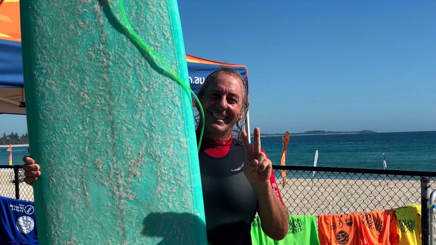 Michael Cottier wears a wetsuit and stands next to a large green surfboard.
