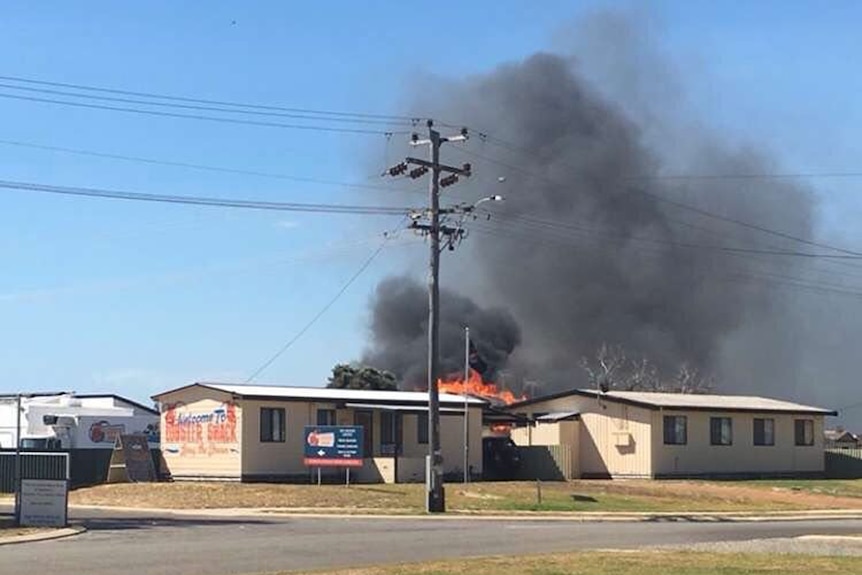 A fire burns behind two weatherboard buildings