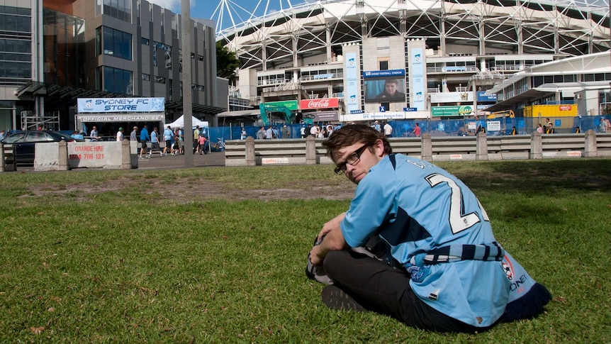A man sitting out the front of the Sydney Football Stadium.