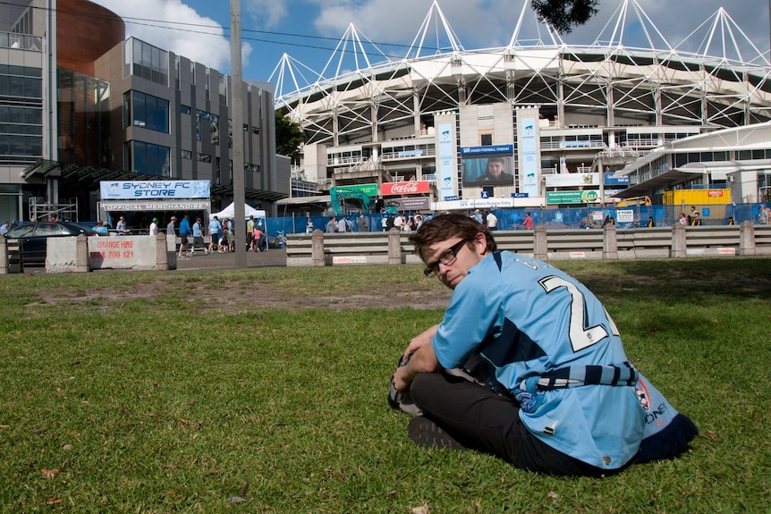 A man sitting out the front of the Sydney Football Stadium.