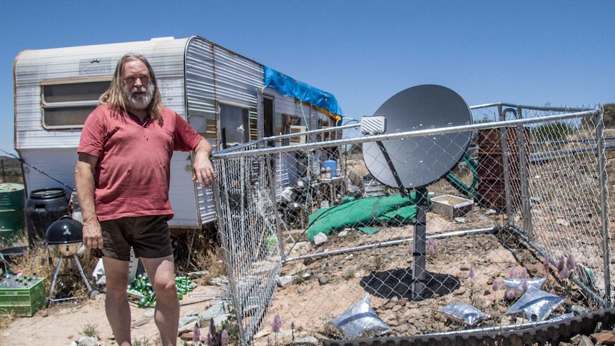 Man standing in front of caravan is accused of illegal camping and fighting council over eviction from his own land
