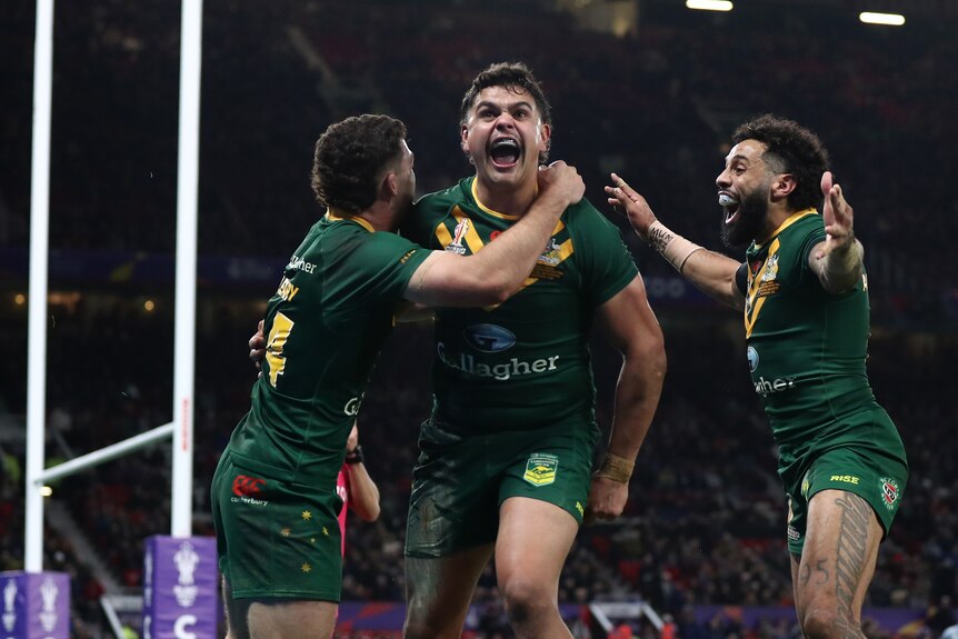 An Australian rugby league player screams in celebration as his teammates join in after a try.