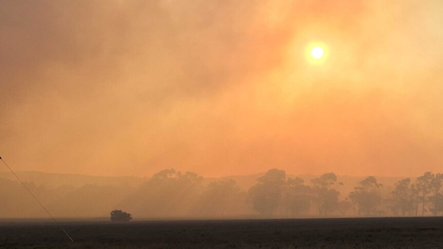 Smoke fills the horizon, shining down on a truck in the fields.