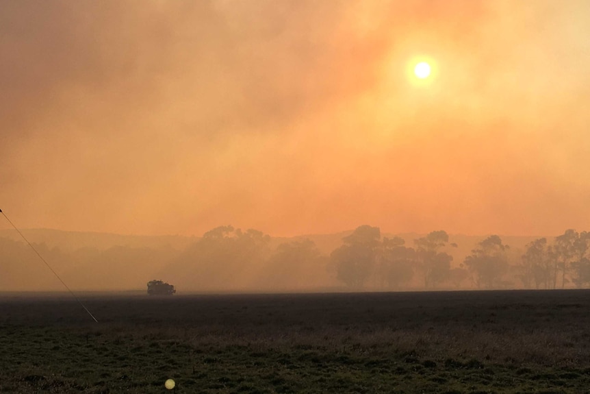 Smoke fills the horizon, shining down on a truck in the fields.