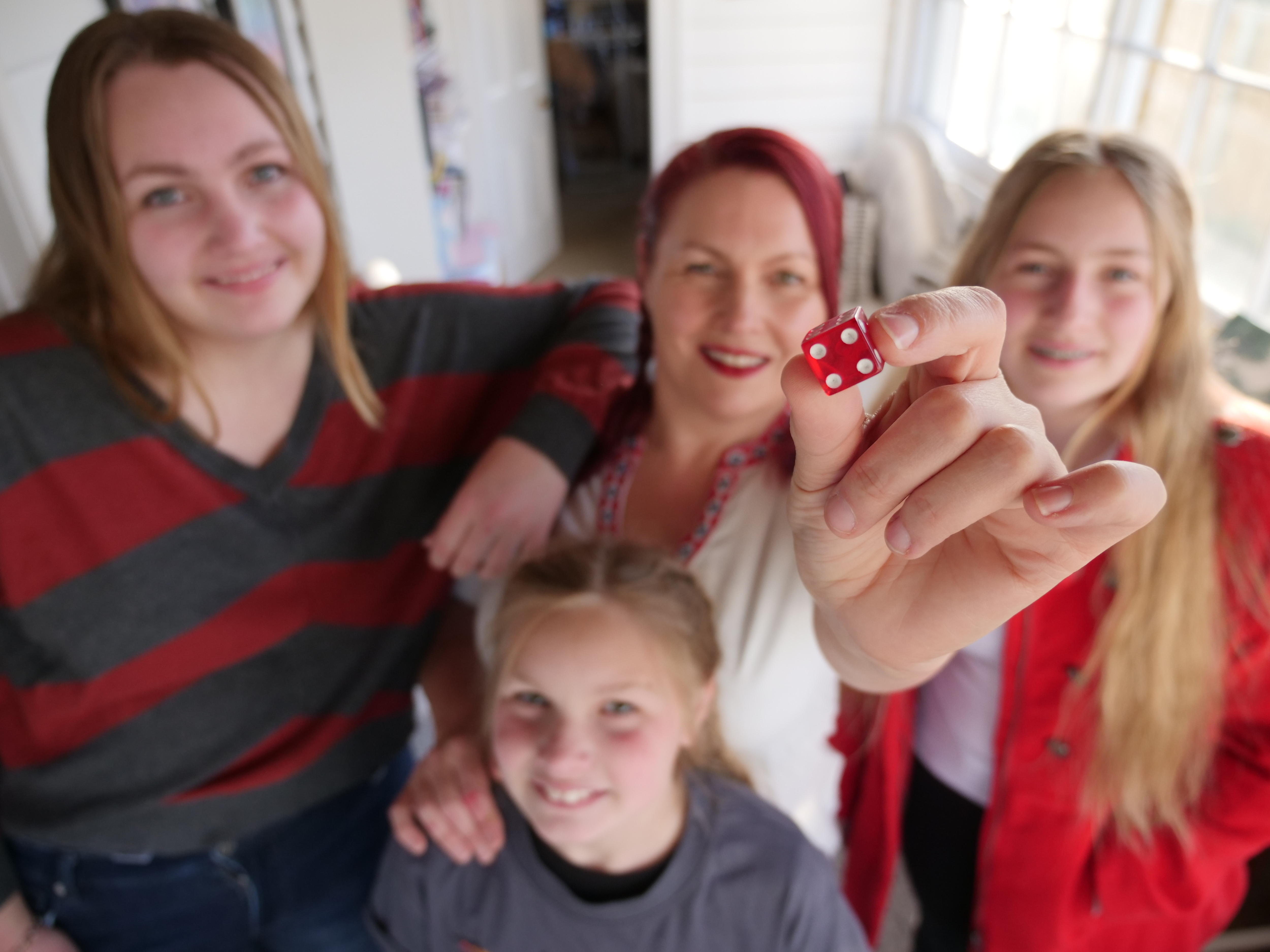 Woman and three girls standing close and smiling as the woman holds a red dice towards the camera.
